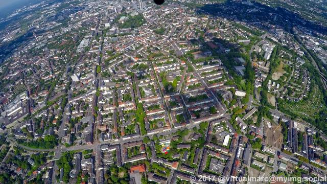 An aerial photo of Essen Rüttenscheid. You see multiple living quaters between rows of trees. The Essen central station can be seen in far distance.