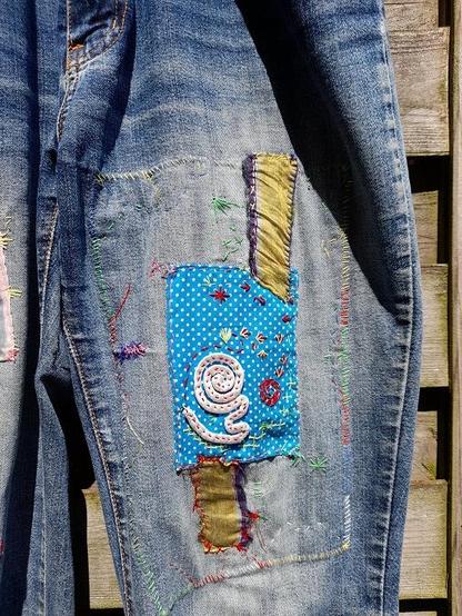 Visible mending on jeans with self-made patches, silk stripes, and wild coloured embroidery.
