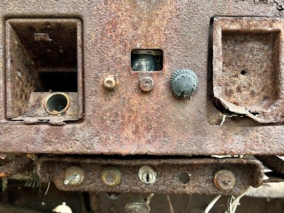Rusty dash of a very old truck (50’s?) with, near as I can make out from left to right
Upper:
* ashtray slot w/hole for lighter
* radio with 3 “knobs” and a peephole view of current frequency
* no idea, rectangle indented plate with small hole
Below that:
* shaft of knob?
* remnant of knob or switch
* slot for key
* empty hole
* another switch or knob remnant

Under dash:
* maybe a pull knob, for choke or vent