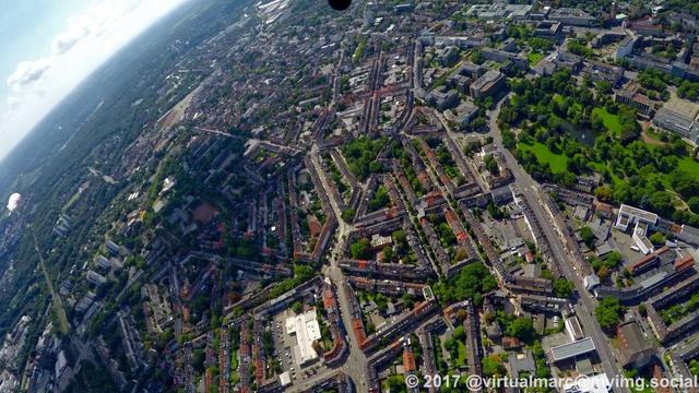 An aerial photo of the center of essen. You can see buildings with trees around and the park of the Aalto-Theatre and the philharmonic. The airship of the WDL Luftschiffgesellschaft mbH is hovering over the city.