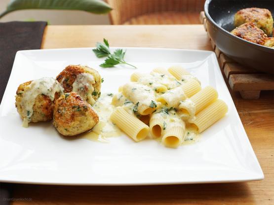 Ein weißer, quadratischer Teller. Auf ihm vegetarische, knusprige Frikadellen und Penne Rigate. Obenauf Kräuterrahmsauce.