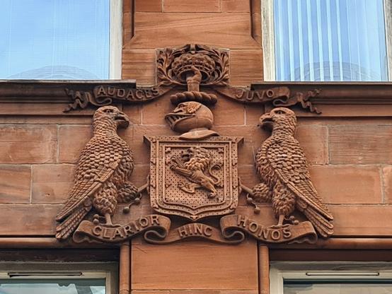 A pair of parrot-like birds supporting a coat of arms of a Glasgow building.