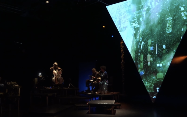 Screenshot aus der Sendung 
düstere Szene mit einigen Musikern und Videoprojektionen auf einer dreieckigen Projektionsfläche