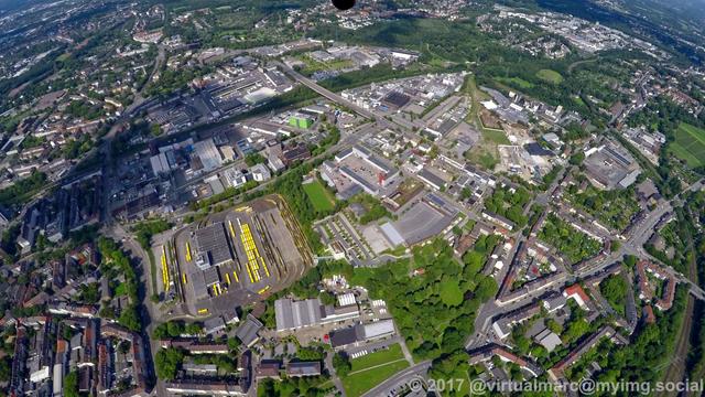An aerial photo of the center of essen, north of the main station. You can see som living but also many working quaters, sourrounded by trees. Theres also one big bus and tram depot of the RuhrBahn (formally EVAG) in the bottom left with yellow busses and trams.