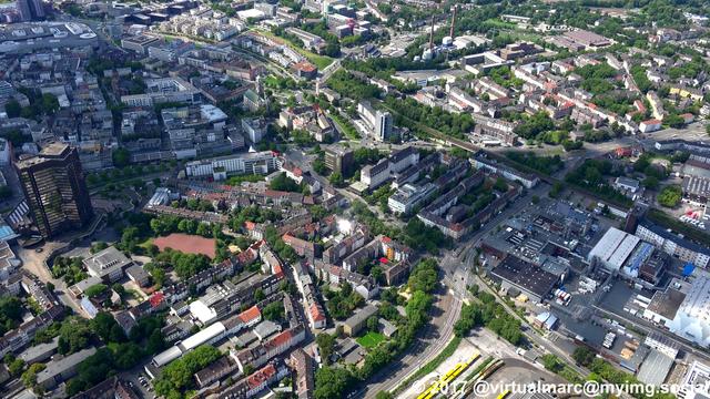 An aerial photo of the center of Essen with living and working quaters sourrounded by trees. A big Y-Shaped black building can be seen on the left, this is the city hall of Essen.