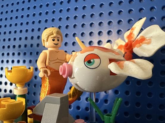 Lego MerStede petting a Goldeen (a Pokémon that looks like a white and orange goldfish with a little horn in its head