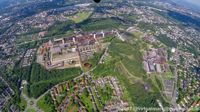 An aerial photo of the unesco world heritage site Zollverein. The coking plant can be seen on the left to middle side, the coal mine on the right side. Sourrounded by many trees and green nature.