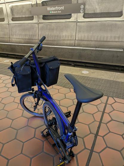 Blue folding bike, half folded (rear wheel folded underneath tube top) sitting on Waterfront metro platform, with the Waterfront sign visible