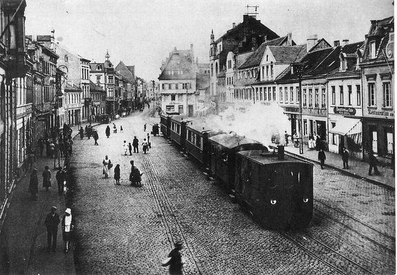 Marketplace of Brühl with steam train of the Cologne-Bonn RR, about 1900. Photo credit: unknown photographer/Public Domain. https://commons.wikimedia.org/wiki/File:Bruehl_Feuriger_Elias.jpg