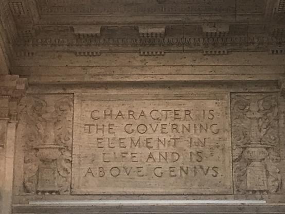 Letters etched into a beige stone wall read (in all caps), Character is the governing element in life and is above genius. Photo taken at the Asian Art Museum in San Francisco;, formerly the city's Main Library.