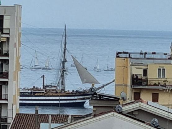 Tra due palazzi fronte mare si vede la nave Amerigo Vespucci che solca il mare