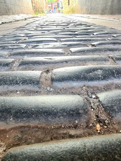 Heavily worn setts lining a pend beneath a tenemwnt building, leading to an open area behind it.