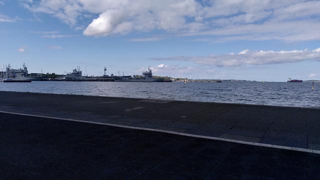Kieler Innenförde Richtung Laboe, Marinehafen links, Leuchtturm Falkenstein in der Bildmitte. Am Himmel ein paar Haufenwolken, auf dem Wasser leichtes Riffelblech und eine handvoll unaufgeregte Segelboote