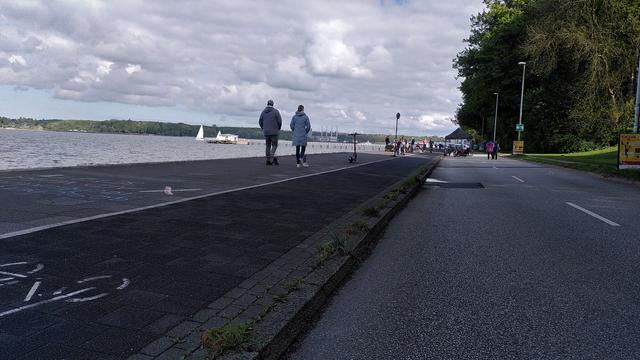 Blick die Kiellinie lang, einlaufend, Menschen auf Gehweg und Straße, im Hintergrund ein Pavilion und mehr Sitzgruppen.