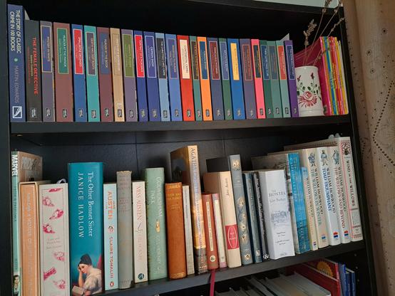 Two shelves with books and a jar of dried lavender in between next to a curtain
