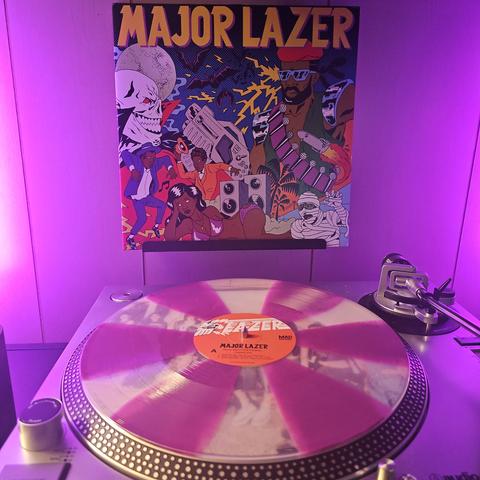 A purple and clear pinwheel vinyl record sits on a turntable. Behind the turntable, a vinyl album outer sleeve is displayed. The front cover shows comic book like illustration a muscular black man standing across from a bald vampire. The cover also features black men dancing, a black woman laying down, speakers, a zombie, and bats.
