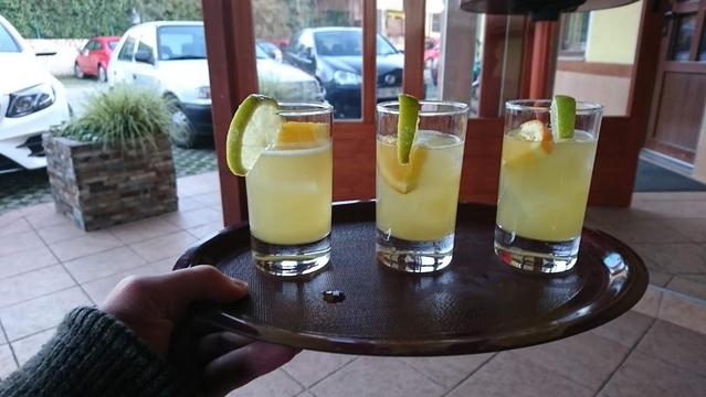 Three cocktail glasses on a tray, garnished with citrus. Hand holding the tray, outdoor setting.
