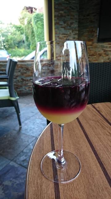 A wine glass filled with a layered drink of purple and yellow liquid on a wooden table.