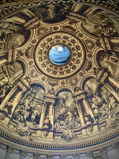 This image features the interior of a beautifully decorated dome, likely from a cathedral or a significant historical building. The dome's ceiling is adorned with intricate frescoes depicting various figures, which could be religious or mythological scenes. Directly at the center of the dome is an opening or an oculus, which allows natural light to illuminate the artwork inside.

The frescoes include detailed images of people in various poses and interactions, set within architectural settings that include columns and arches. Surrounding the central opening are decorative patterns and designs that embody a classical style, with elements like rosettes and detailed moldings, adding to the ornate and grand atmosphere of the space. The mix of art and architecture highlights the skill and aesthetic sensibilities typical of Renaissance or Baroque periods.
