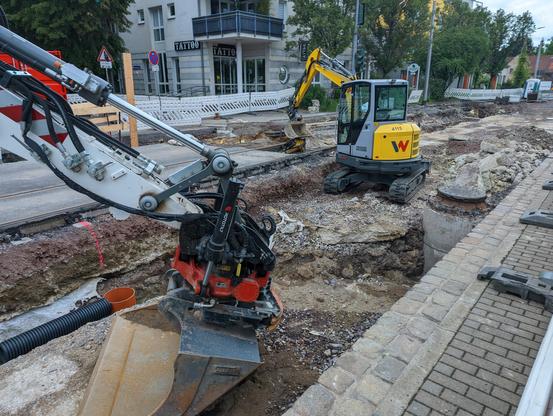 Eine aufgerisse Straße. Ein Kleinbagger und eine weitere Baggerschaufel sind zu sehen. Keine Arbeiter, da Sonntag.