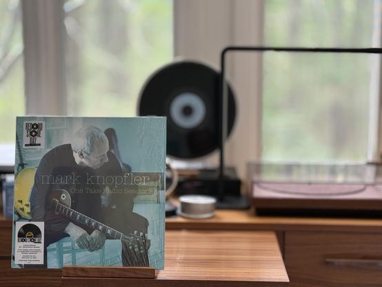Mark Knopfler - One Take Radio Sessions (RSD25) LP cover.

Mark, sitting on a chair, holding his guitar, looking down and to his left.

The black LP plays on a Miniot Wheel 2 turntable to the right.