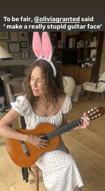 Instagram Story with a photo of Minnie Driver wearing a white and pink bunny ear headband while playing guitar with her mouth slightly open and her eyes closed. She is sitting on a wooden chair in what looks like someone's living room. Text above the photo reads, “To be fair, @ OliviaGranted said ‘make a really stupid guitar face’.”