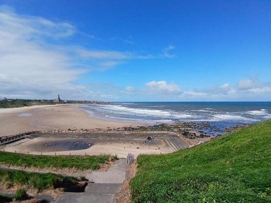 Tynemouth longsands. There is the north sea, golden sands, green dunes, and an abandoned swimming pool.
