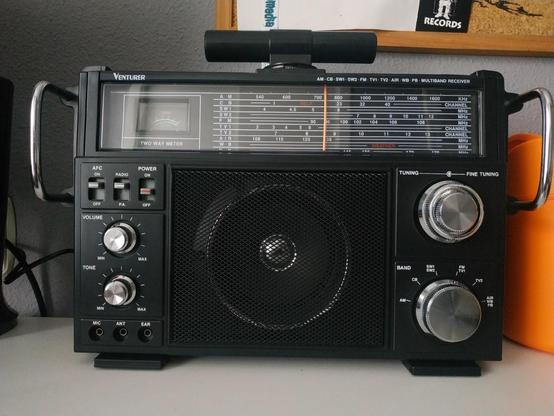 La imagen muestra un receptor de radio multibanda de color negro con botones plateados.