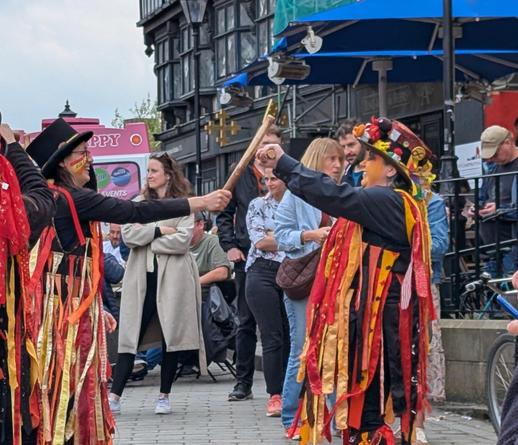 Me and another member of Powderkegs. I am holding my stick up horizontally as she clashes her stick at the centre of mine. We are both laughing.
