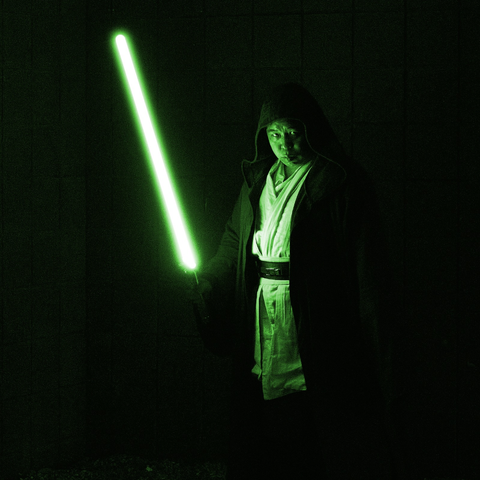 A photograph of me in cosplay as a Jedi from the Star Wars series with a green lightsaber as the only light source for the photography, casting a green light across the whole frame.