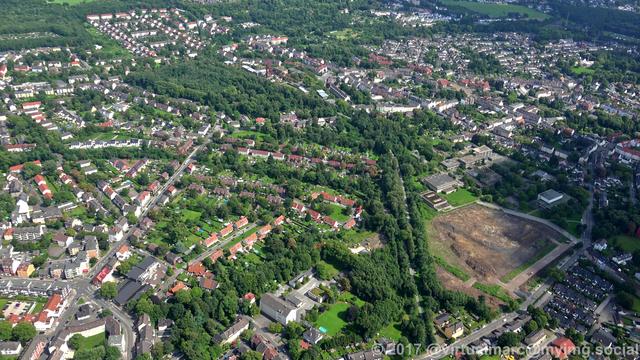 An aerial view of Essen Katernberg, the Zollverein shaft 3/7/10 near the Phenomania Experience Field can be seen in the distance. There are many houses and trees around.