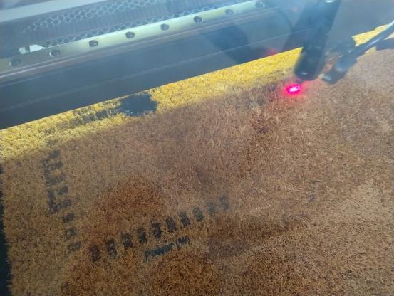 Kokosmatte im Lasercutter der Testmuster einbrennt. Bei einem der Muster gibt es einen großen schwarzen Fleck.