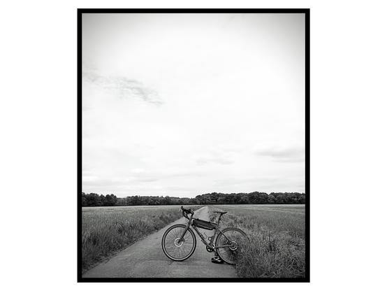 Black and white picture of a gravel bike standing across a country road. Fields on both sides of the road and two third of the picture is taken by the sky.