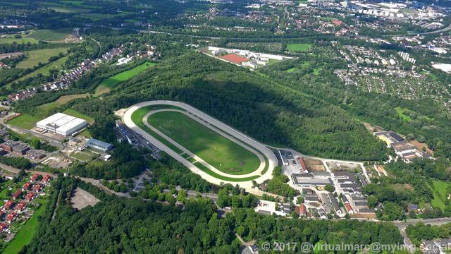 An aerial photo of the harness racing track in Gelsenkirchen with trees around it. The Gelsenkirchen prison can be seen in the distance.