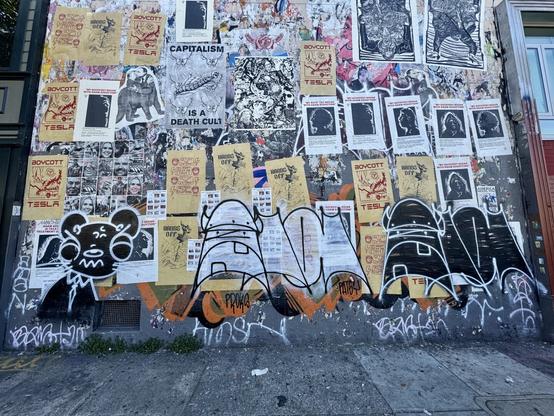 A photo of the "free speech wall" on Valencia Street in San Francisco. It's covered with protest posters and other graffiti. In this photo, you can see one Weasl tag, and two Ola tags.
