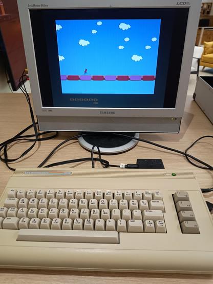 A Commodore 64G connected to a Samsung LCD monitor. A very basic, not working properly, sideways scrolling "endless runner" is on the screen.
