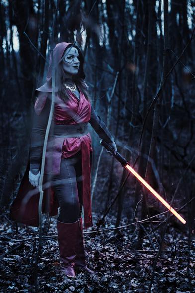 Foto von Lili im Wald. Ihre Haut ist grau mit Bodypaint, sie hat schwarze Gesichtstattoos, ein rotes Outfit samt rotem Lichtschwert. Das Cosplay einer Schwester der Nacht aus Star Wars.