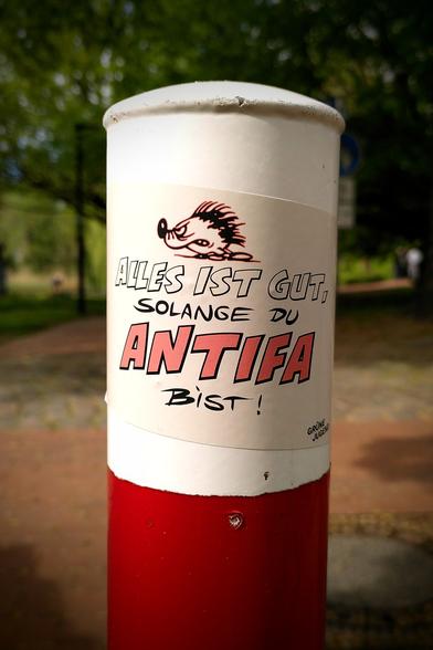 Ein Aufkleber an einen rot-weißen Begrenzungspfahl eines Fußweges.
Darauf ein entschlossen, wütend aussehender Igel. Darunter steht: " Alles ist gut, solange du Antifa bist!". Unten in der Ecke: "Grüne Jugend".