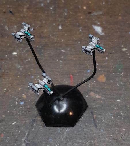 three tiny spacefighter miniatures on black paper clips, boring grey with turquoise canopies