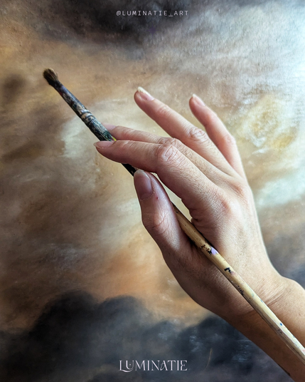 Photographie de la main de l'artiste peignant un tableau acrylique d'un ciel nuageux aux couleurs ocres.
