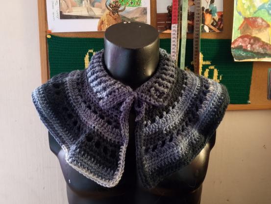 Cuello con pechera tejido a crochet en tonos degradados de gris y negro, con diseño de puntos calados y borde recto. Se ajusta al cuello mediante un lazo delantero.
