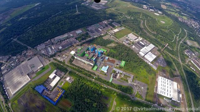 An aerial photo of the Waste-fired power plant in Herten. The spoil heap Hoppenbruch with a wind turbine on the top can be seen in the top left and the Hoheward spoil heap with the Horizon Observatory can be seen in the top right. There are trees all around.