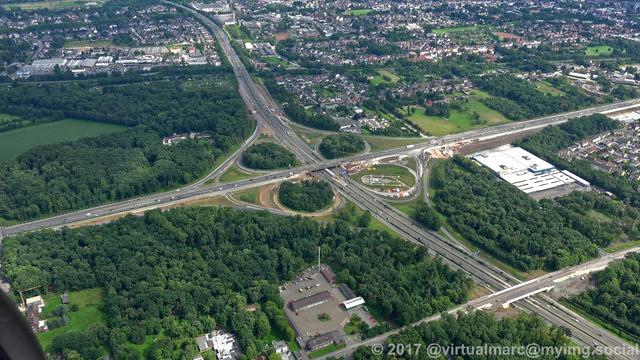 An aerial photo of a Cloverleaf crossing between two freeways in recklinghausen sourrounded by trees.