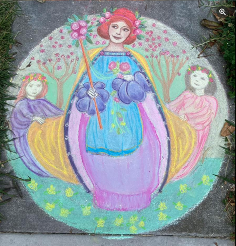 A colorful chalk drawing on pavement, of three figures meant to resemble a May Queen and her attendants, in a circle frame. The May Queen is holding a wand of flowers and a bouquet; she also has flowers in her red hair.