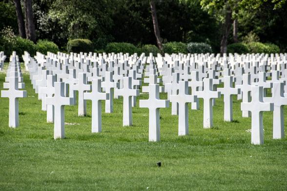 American Cemetery in Omaha Beach. Many crosses, all white, all identical, on a green field. Trees at the back.