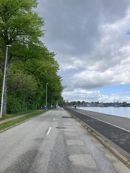 Blick eine Uferstraße entlang, ohne Autos nur vereinzelte Personen