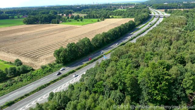 An aerial photo of the freeway A43 from a lower dinstance since we are preparing to land on the runway of the Marl Lohemühle airport. There are trees and a farm yard around the freeway.