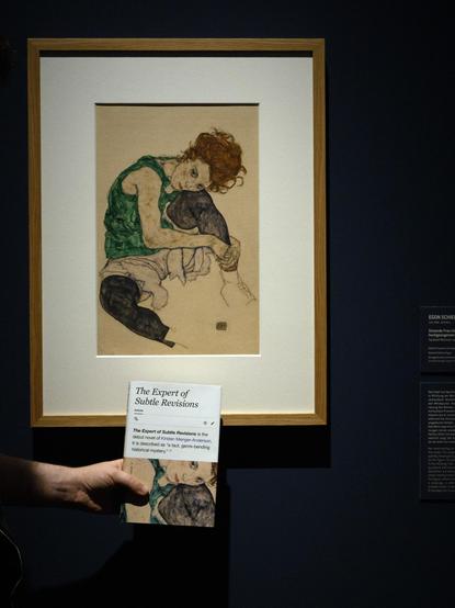 A photograph of the novel The Expert of Subtle Revisions by Kirsten Menger-Anderson with the painting Seated Woman with Bent Knees by Egon Schiele, taken by photographer Elisabeth Preininger, Vienna, Austria. (@Elisabeth_P)
