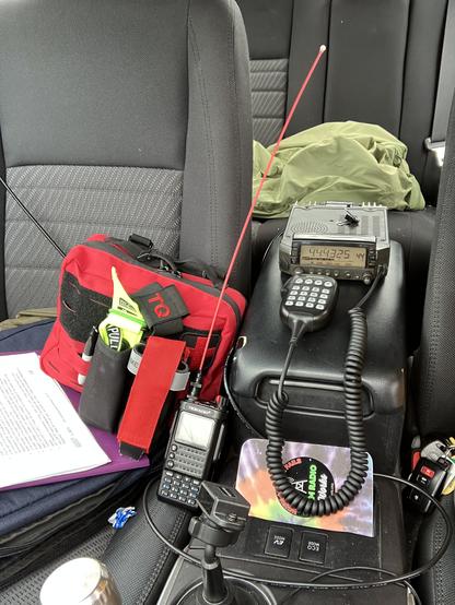 the front passenger side and center arm rest console of a car. Two radios and a red first aid kit are visible.