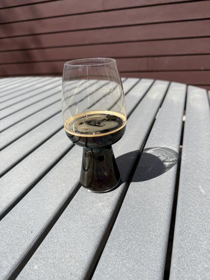 A stout glass of dark beer on a grey picnic table bathed in bright sunlight